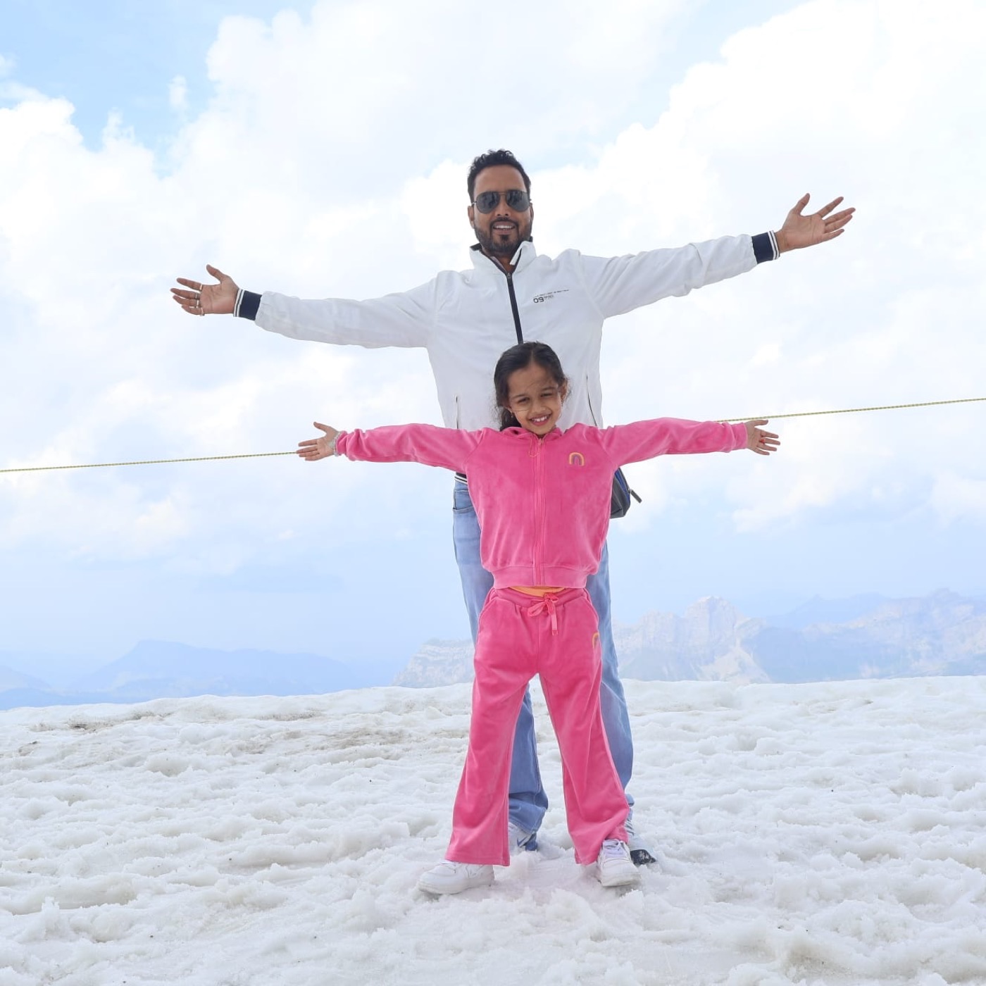 A father and daughter with arms outstretched on an alpine summit
